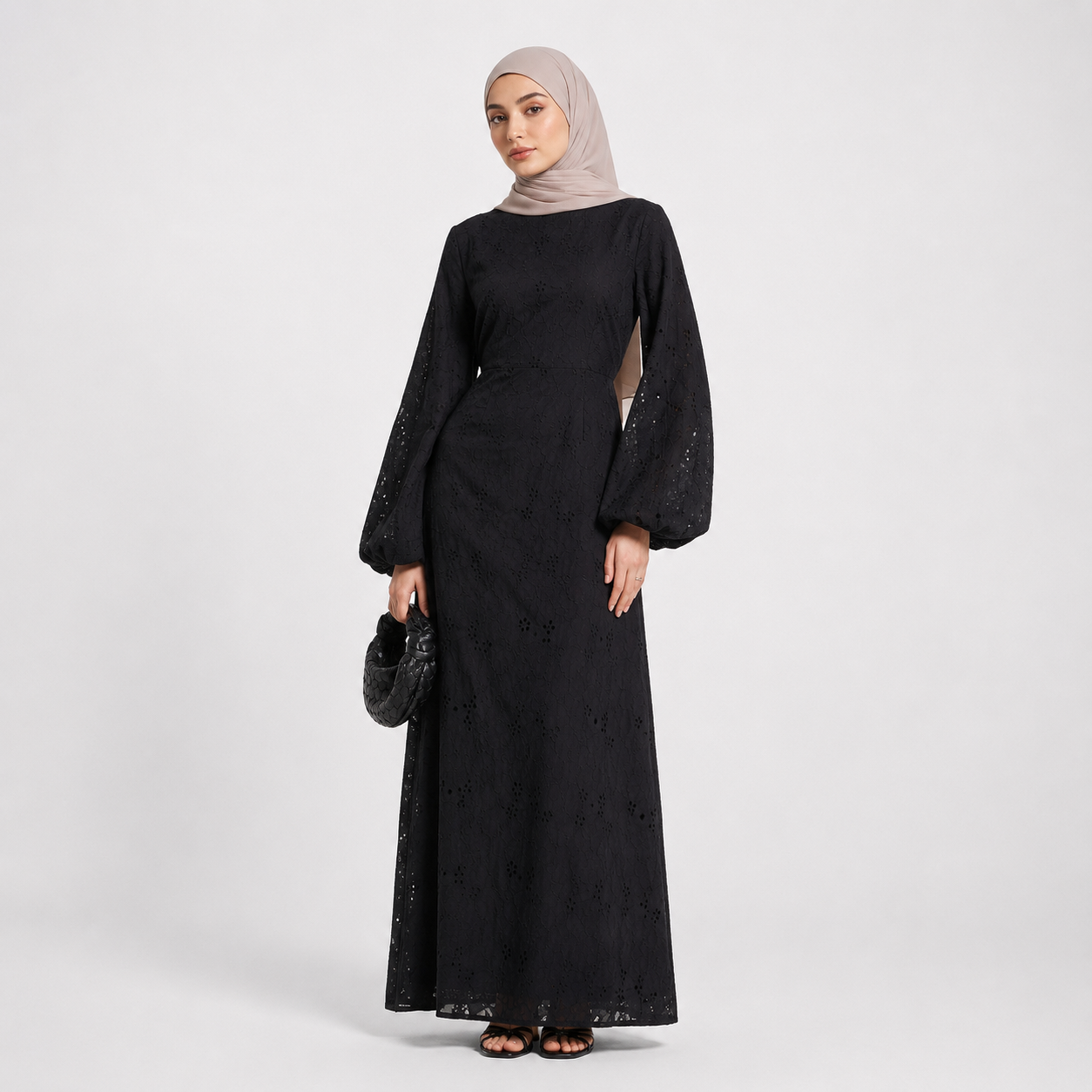 Woman wearing a black dress with long sleeves and a beige hijab on a white background