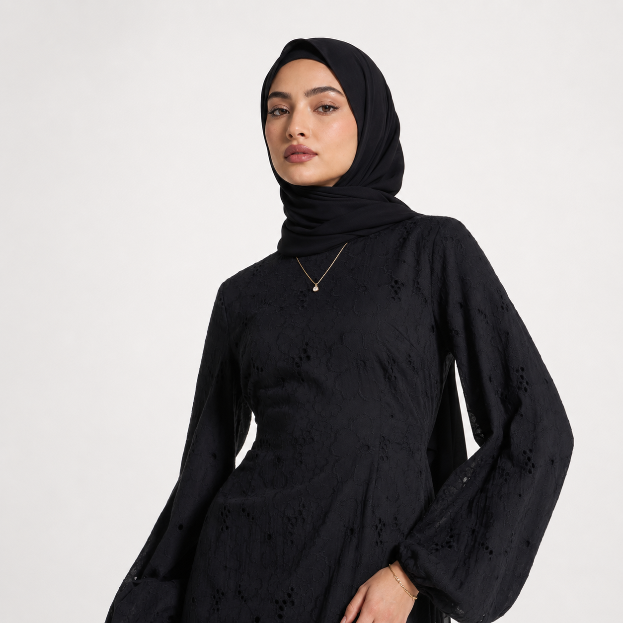 Woman wearing a black hijab and black dress on a white background