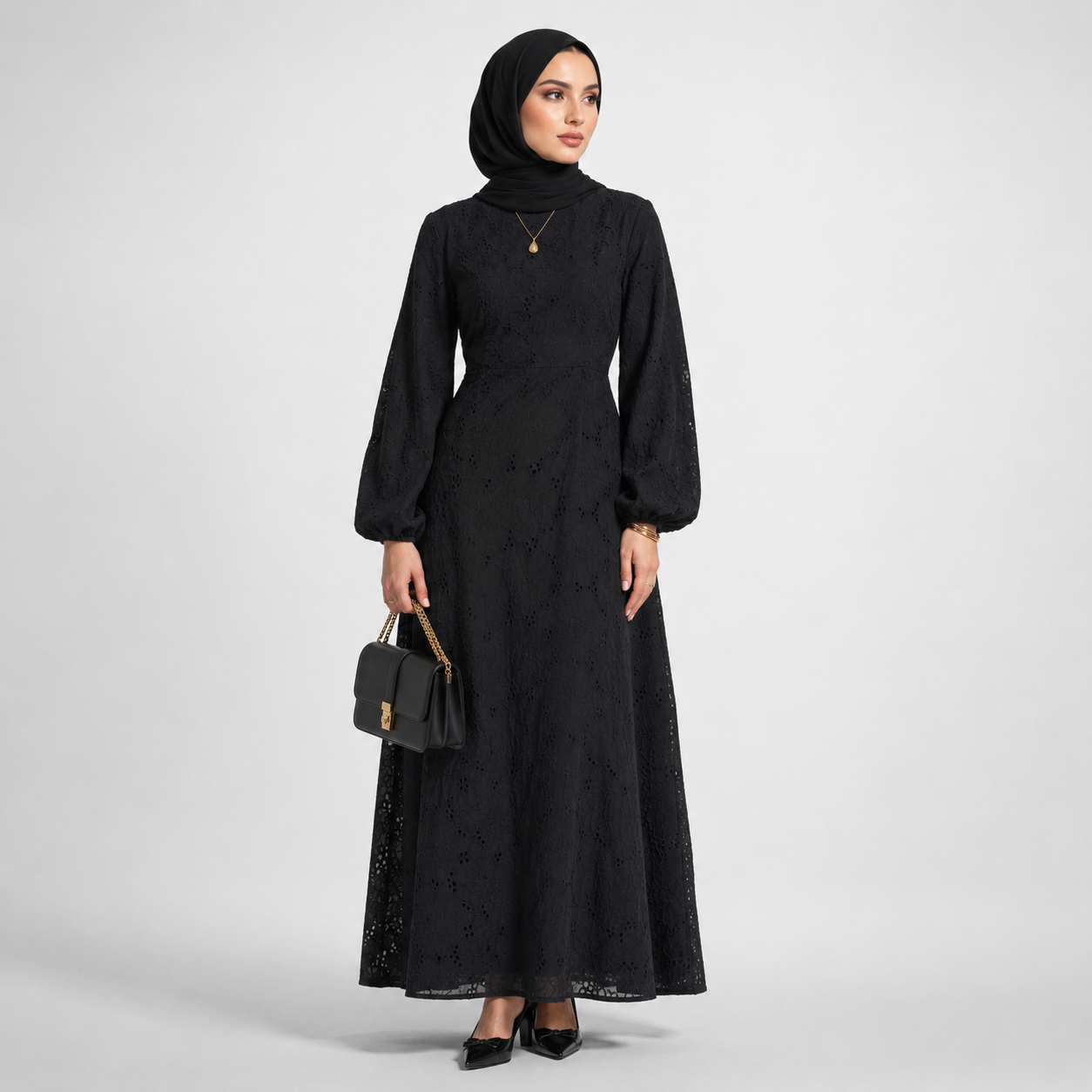 Woman wearing a black dress with long sleeves and a matching hijab on a white background