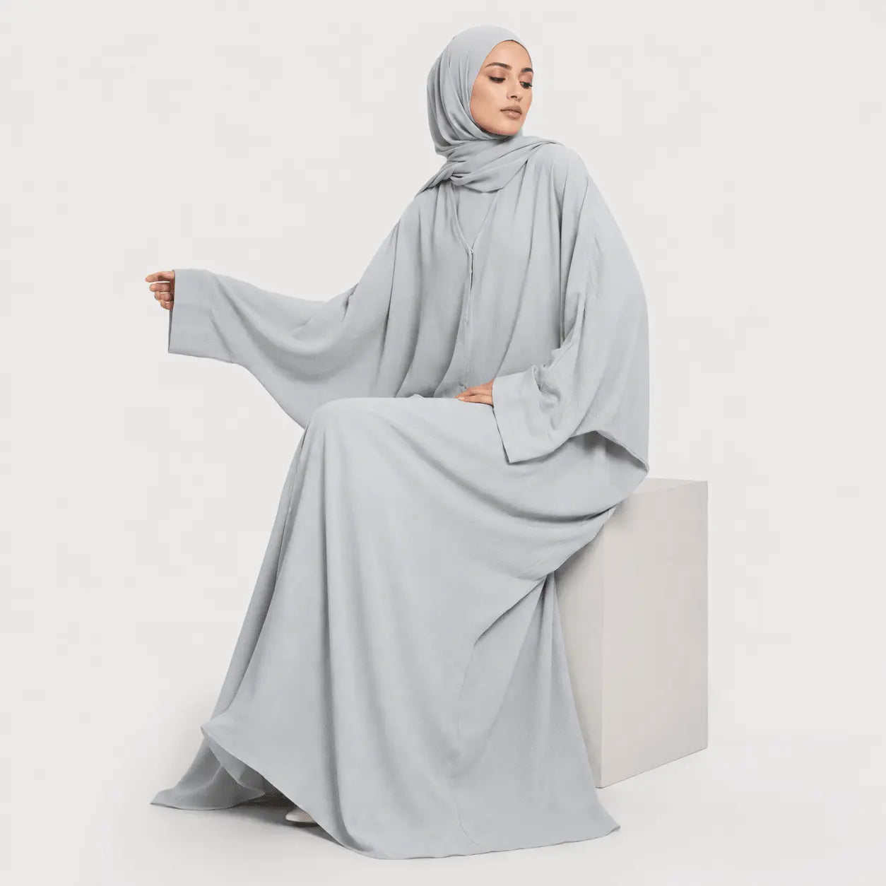 Woman wearing a light gray abaya and hijab on a white background