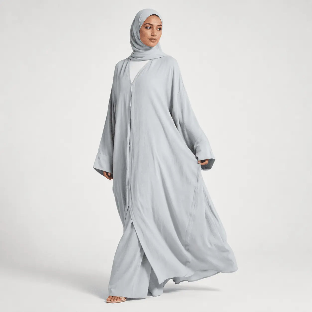 Woman wearing a light gray abaya and hijab on a white background