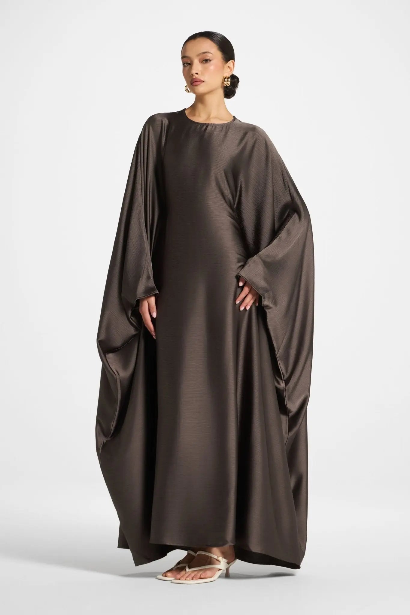 Woman wearing a brown long dress with wide sleeves on a white background
