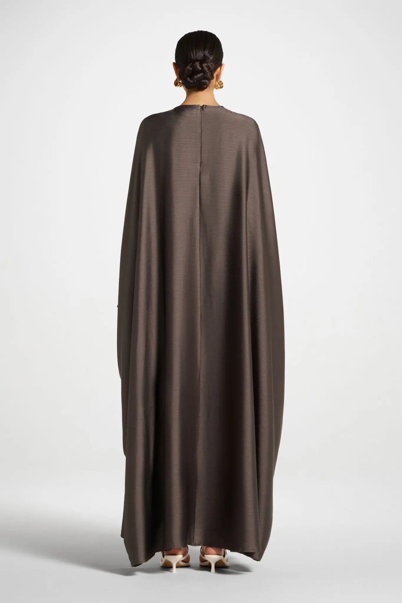 Person wearing a brown cape from behind on a white background