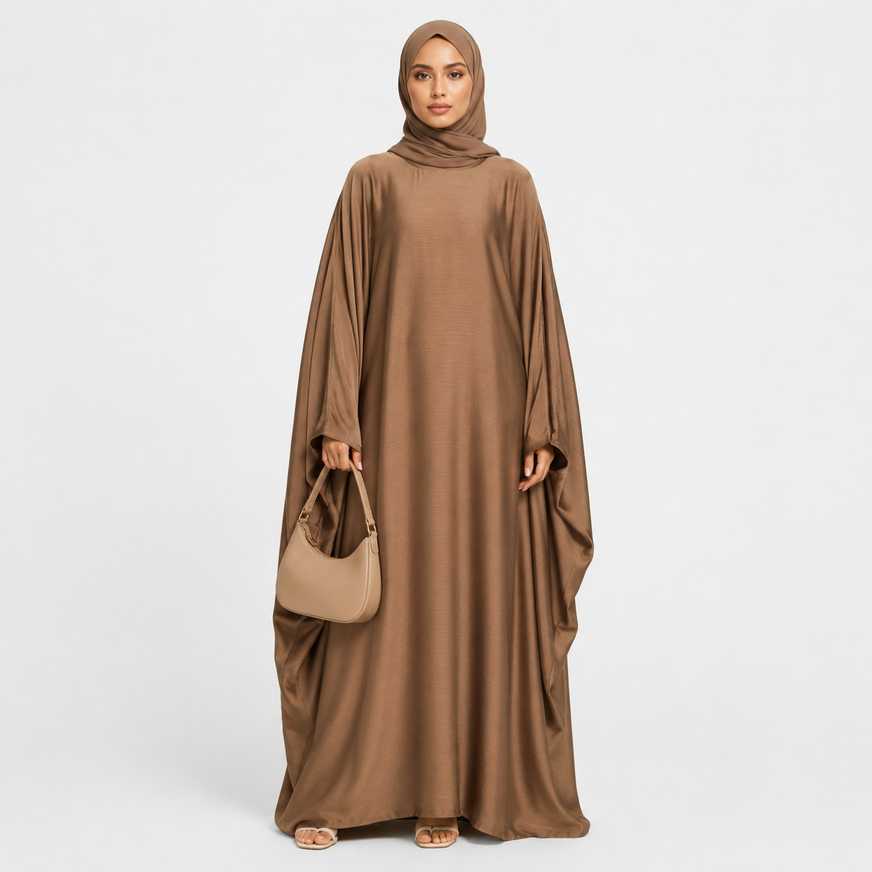 Woman wearing a brown abaya holding a matching handbag on a white background