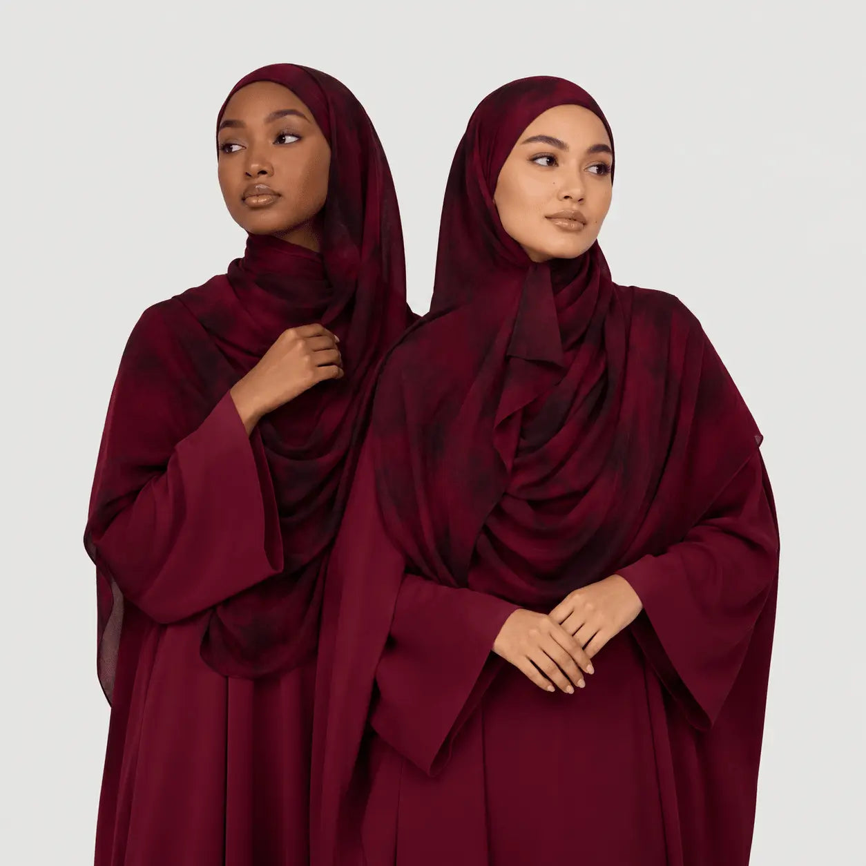 Two women wearing burgundy abayas against a white background