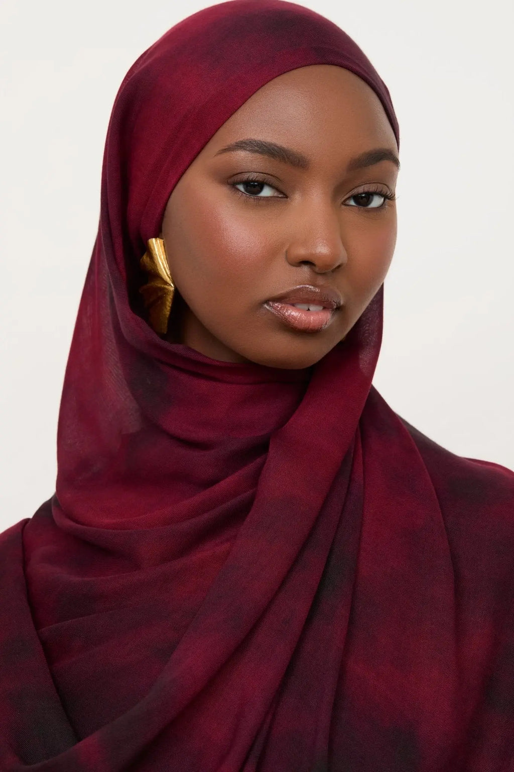 Woman wearing a maroon hijab against a white background