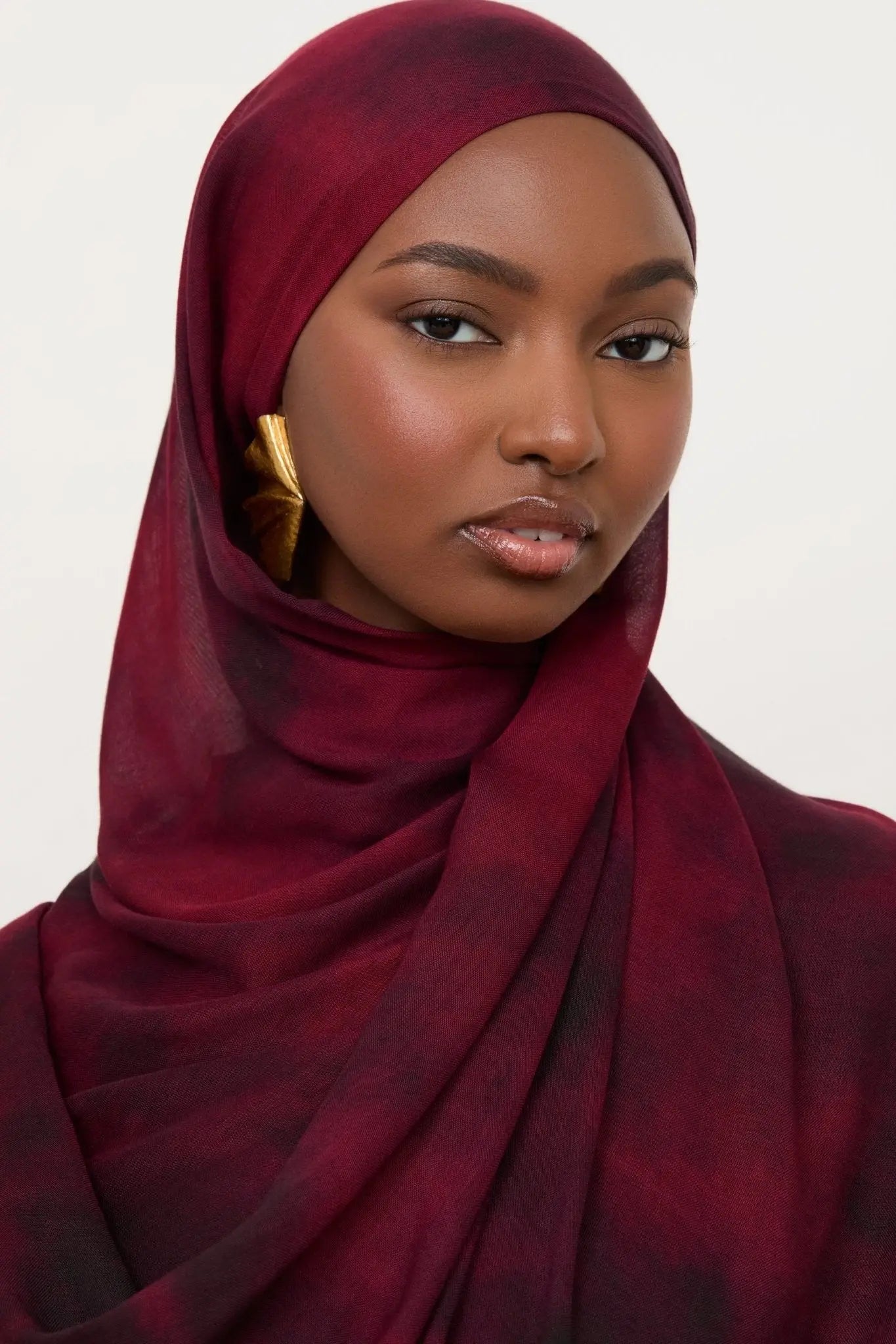 Woman wearing a maroon hijab against a white background