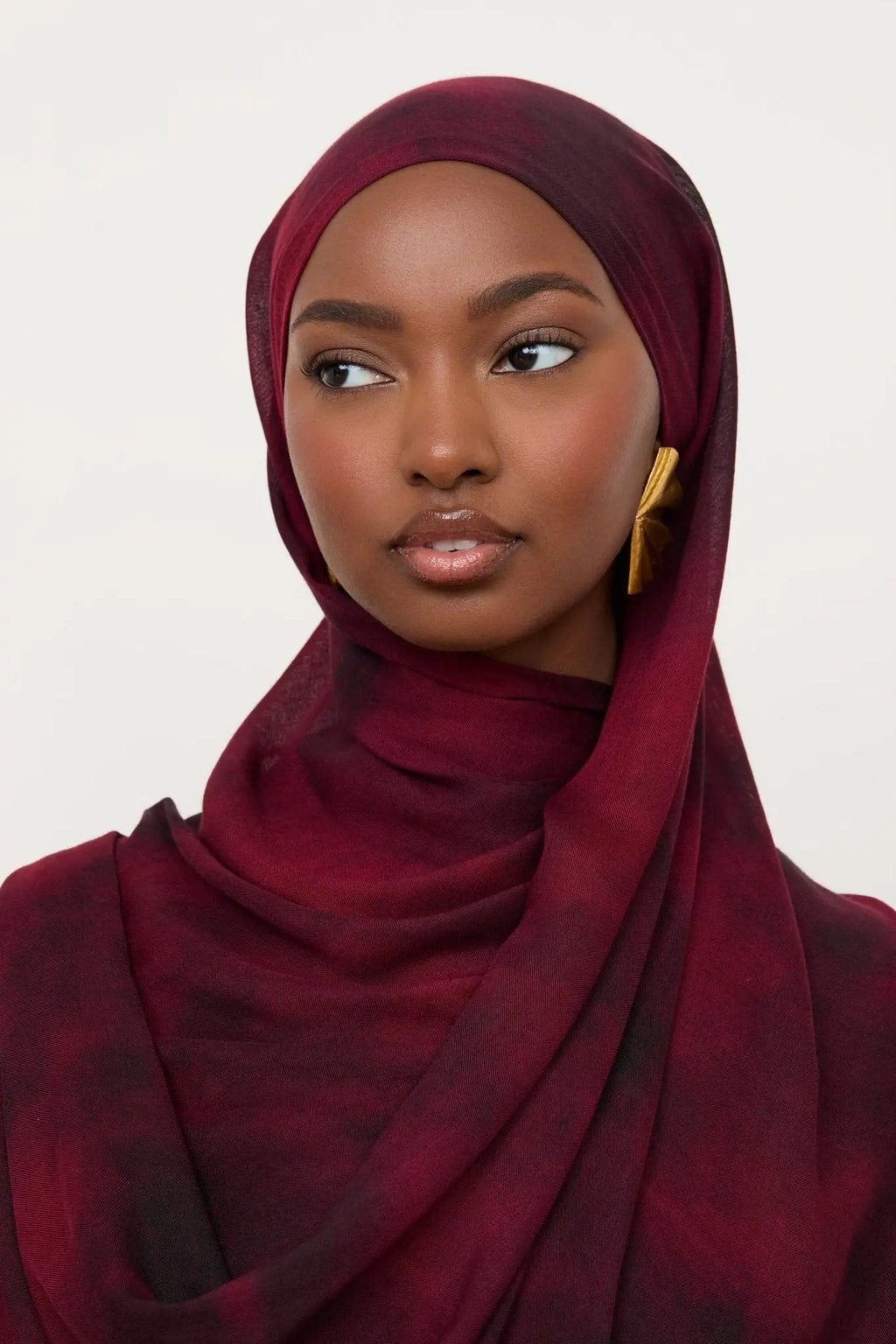 Woman wearing a burgundy hijab against a white background