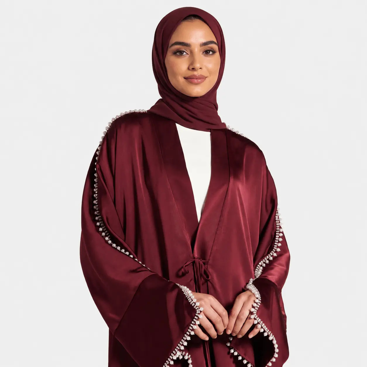 Woman wearing a burgundy abaya with white trim on a plain background