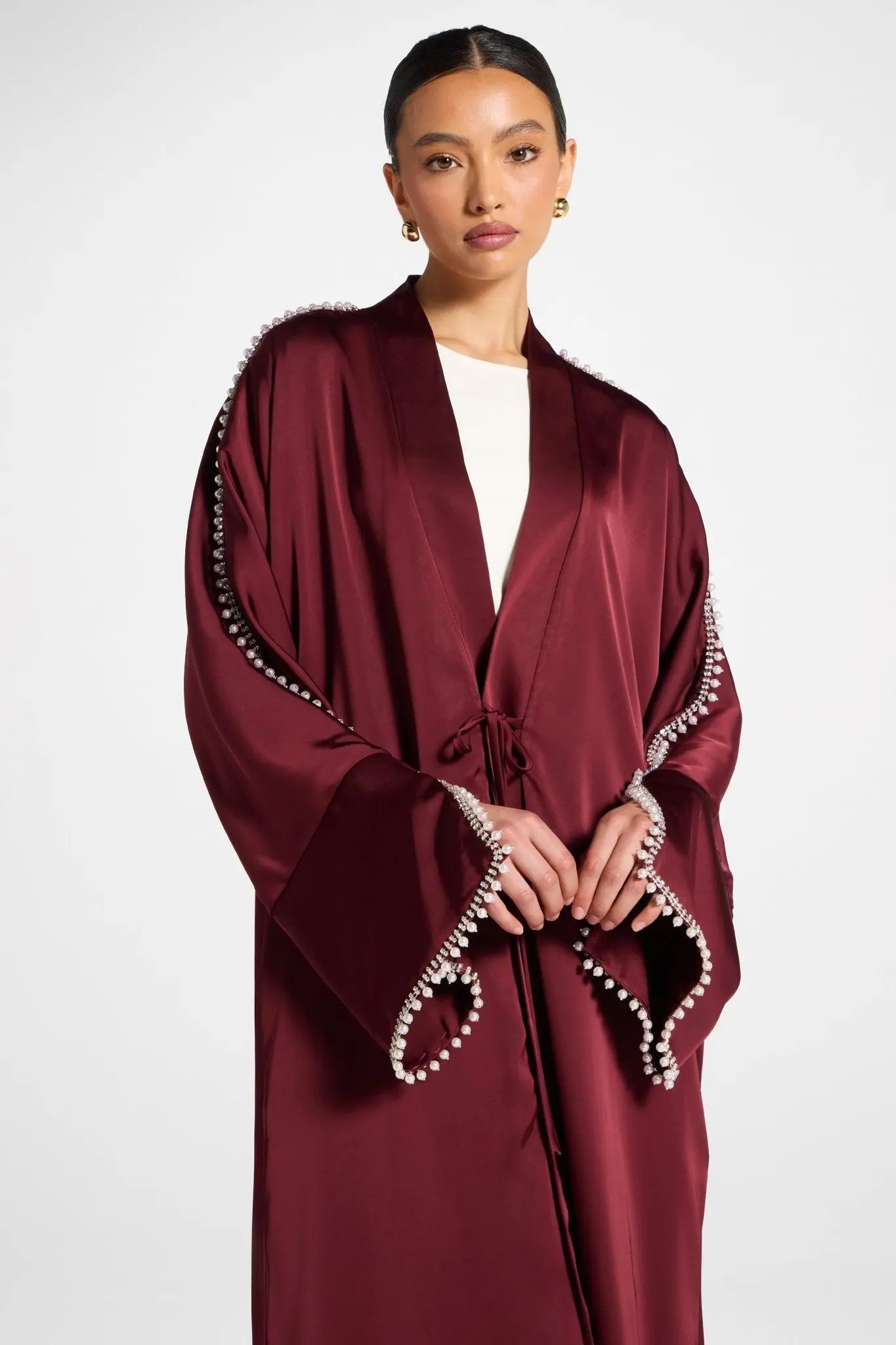 Woman wearing a burgundy abaya with decorative trim on a white background