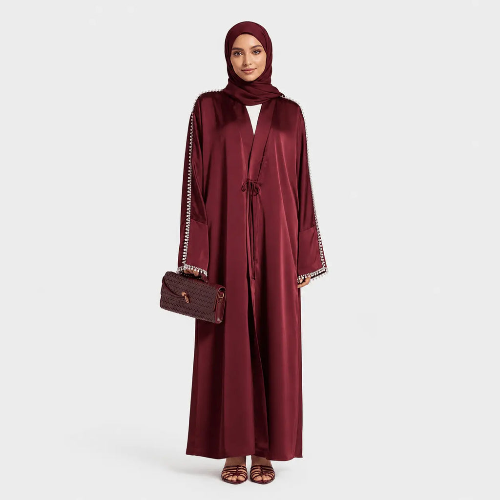 Woman wearing a burgundy abaya with a matching headscarf on a white background