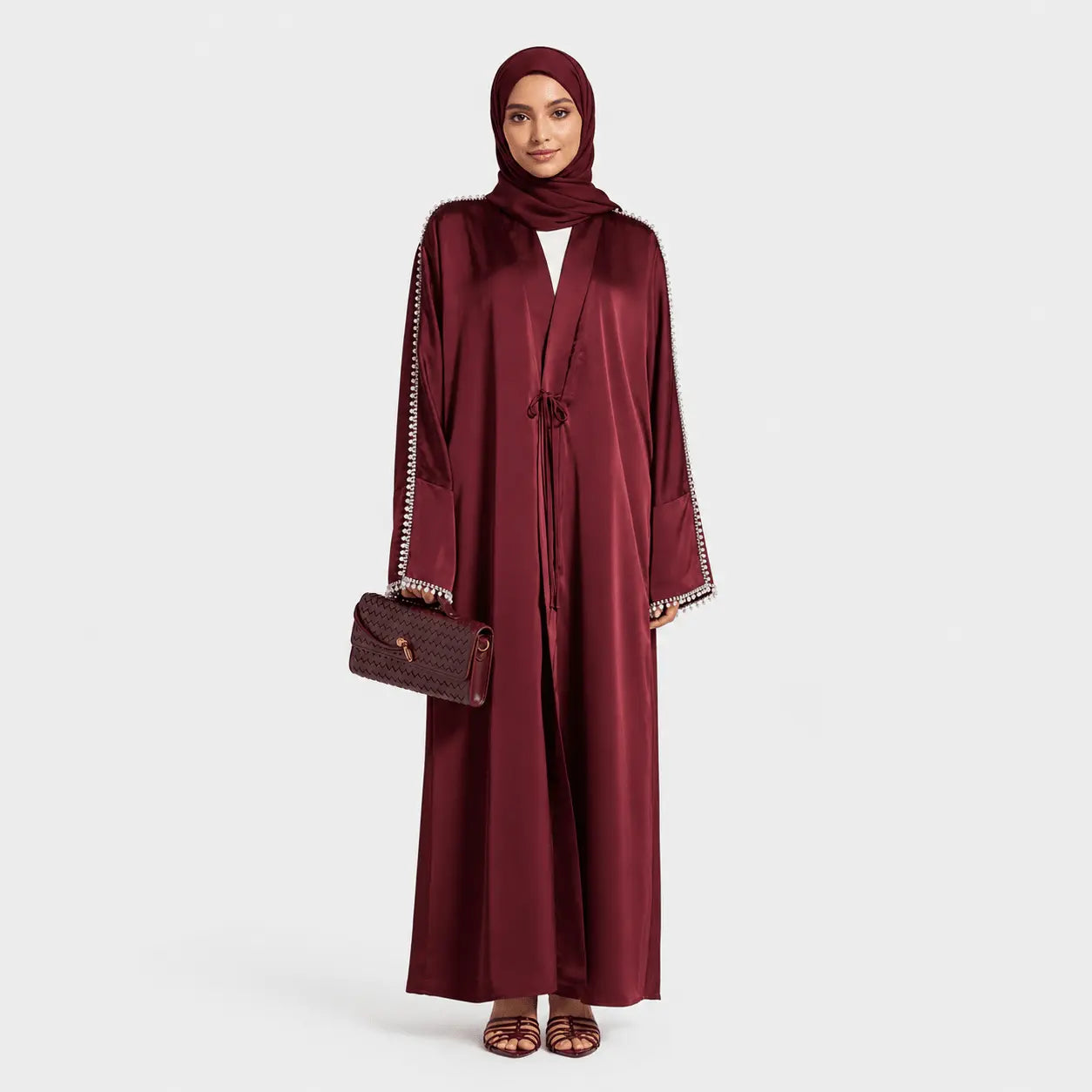 Woman wearing a burgundy abaya with a matching headscarf on a white background