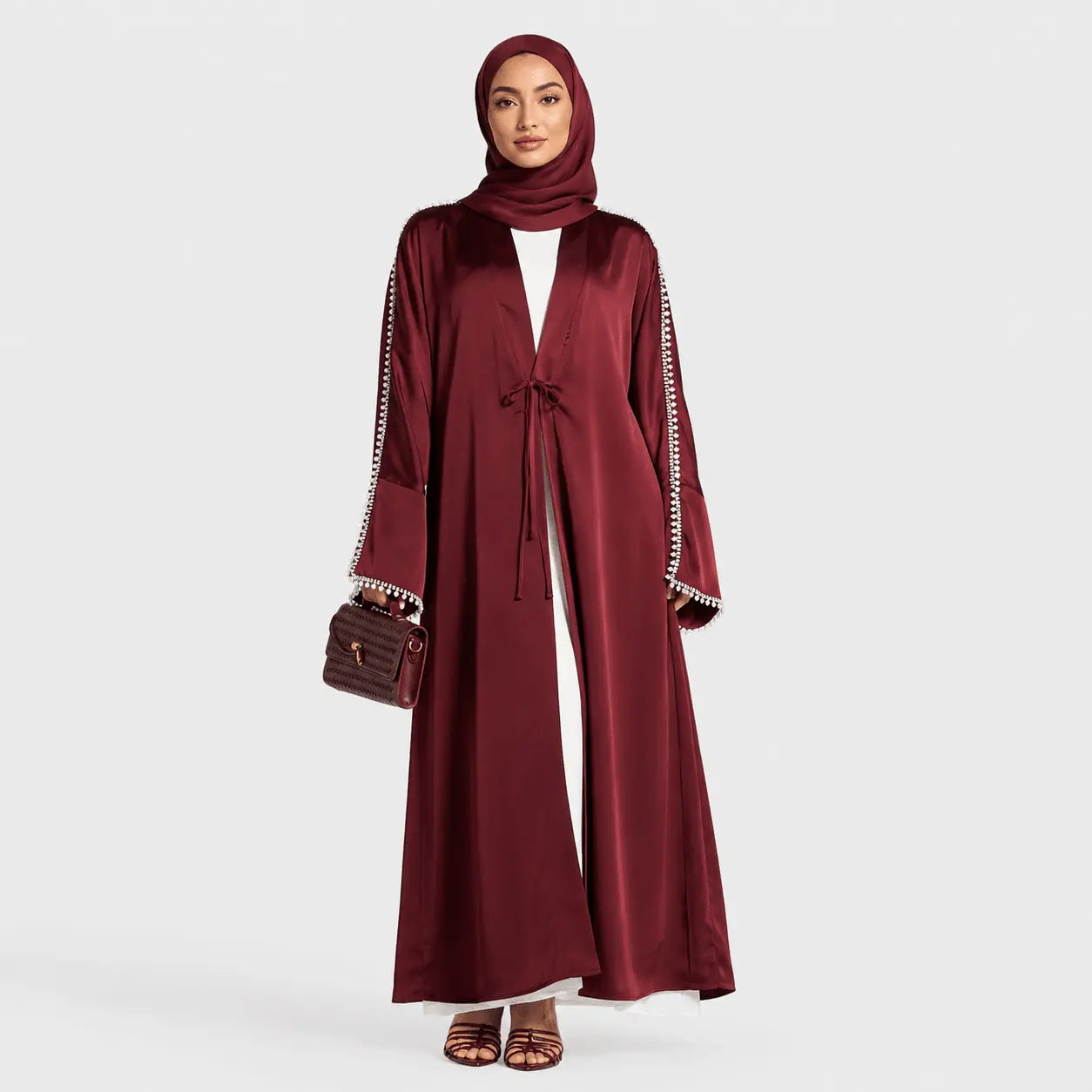 Woman wearing a burgundy abaya with a matching hijab on a white background