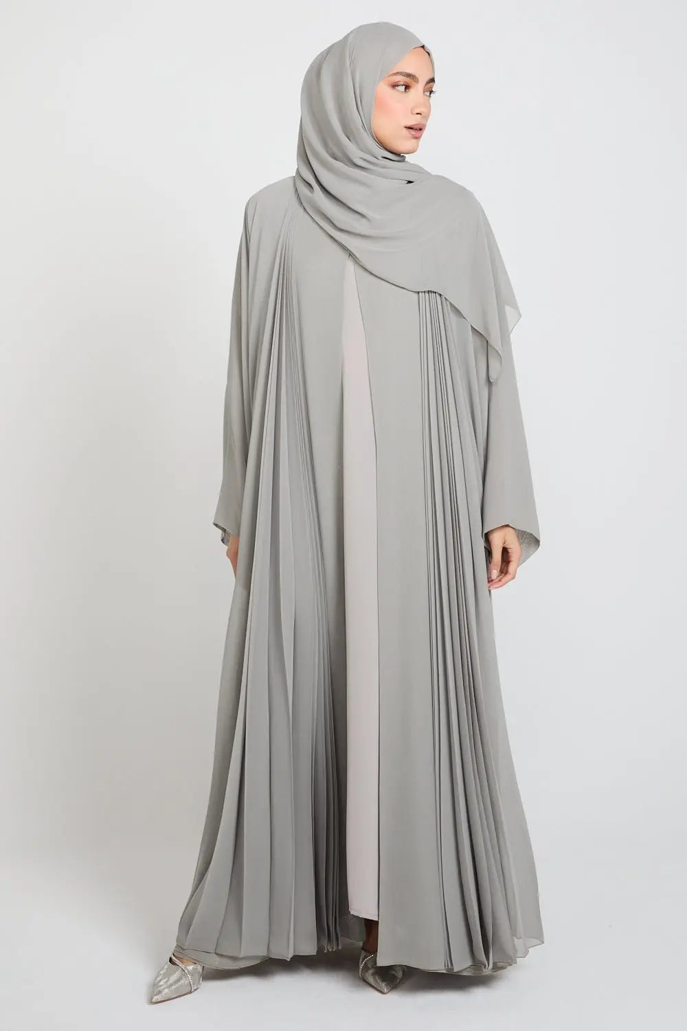 Woman wearing a light gray abaya with a matching hijab on a white background