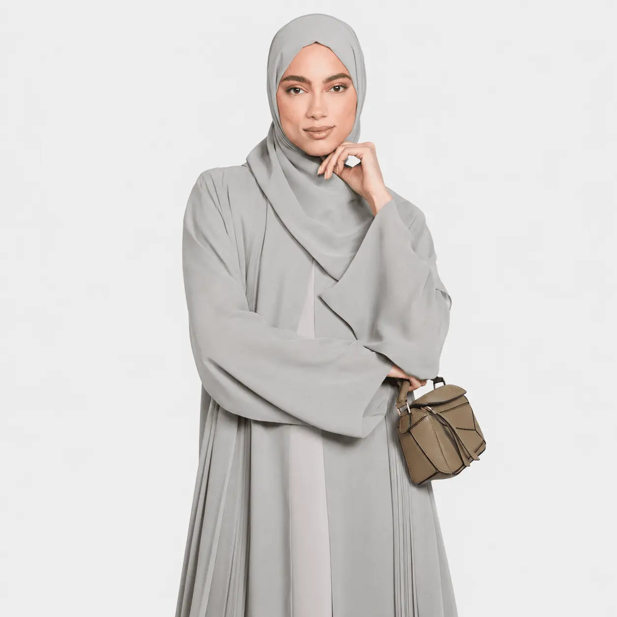 Woman wearing a gray abaya with a beige bag on a white background