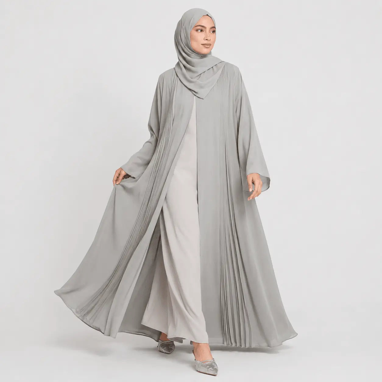 Woman wearing a long gray hijab and white dress on a light gray background