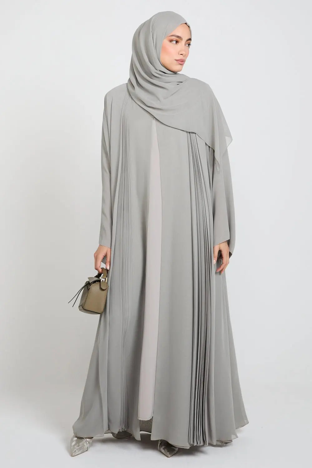 Woman wearing a long, light gray dress with a matching hijab on a white background