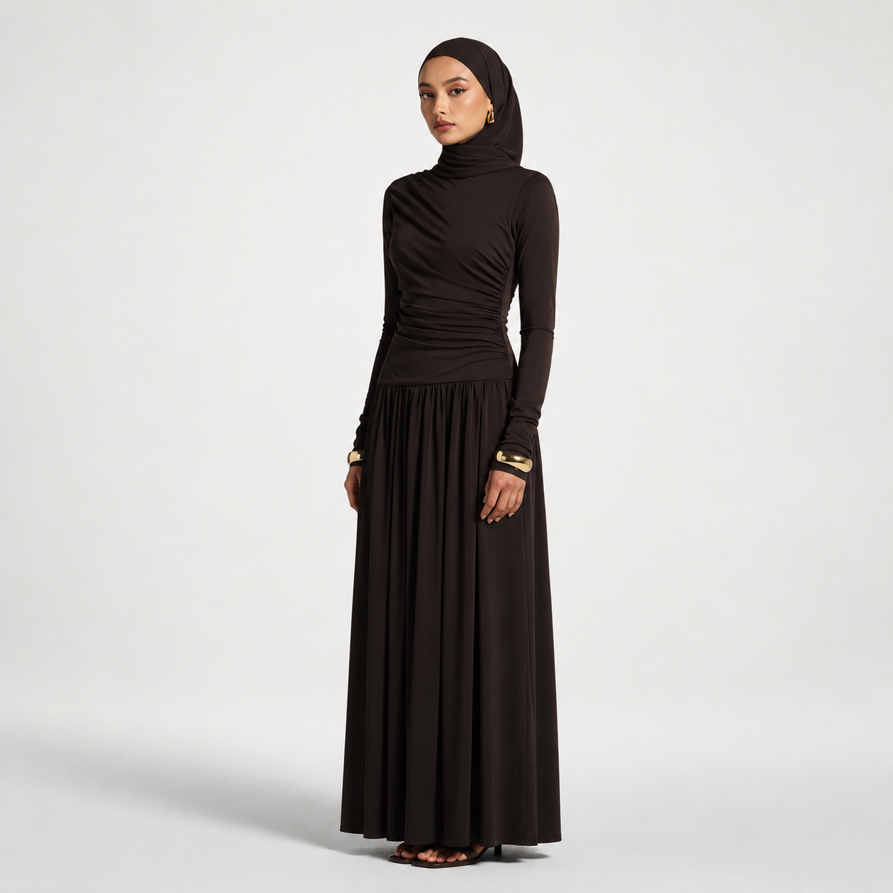 Woman wearing a long black dress with a matching hijab on a white background
