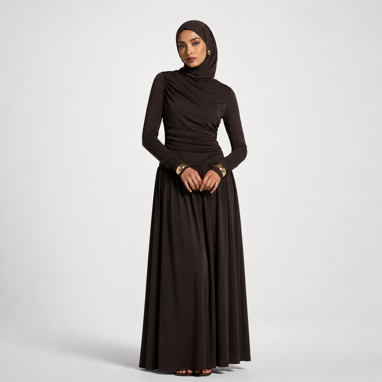 Woman wearing a long black dress with a matching hijab on a white background