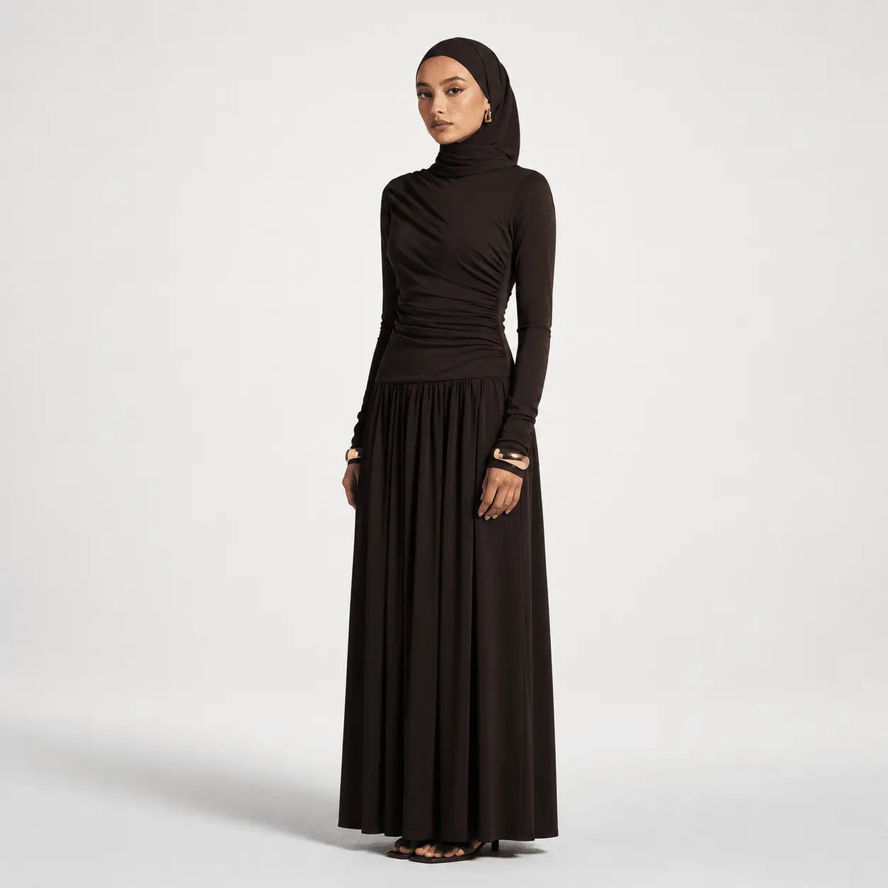 Woman wearing a long black dress with a matching hijab on a white background
