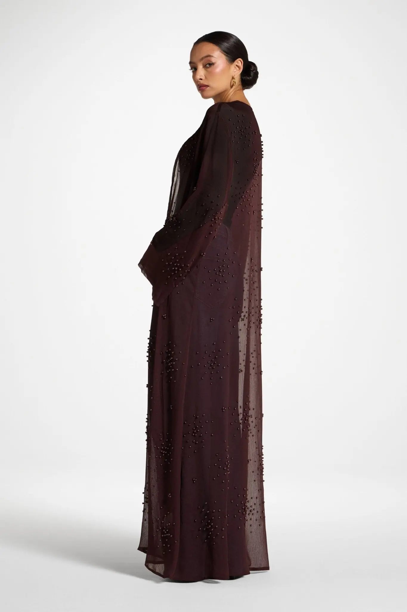 Woman wearing a long, dark brown dress with lace details on a white background