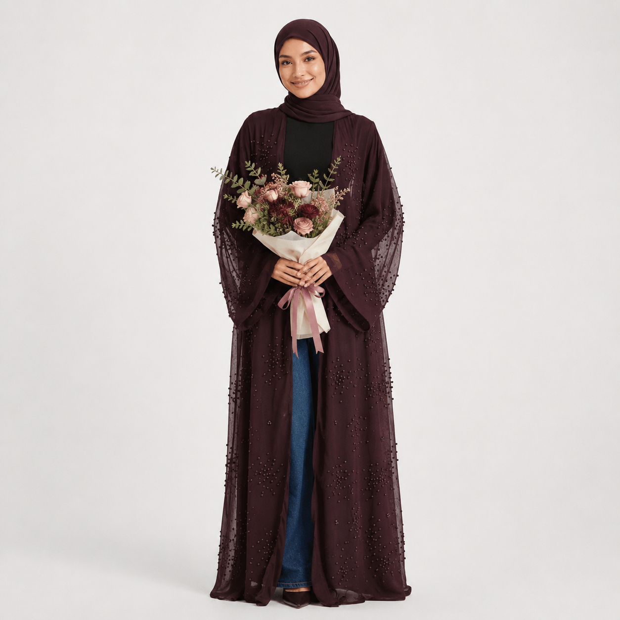 Woman wearing a dark brown abaya holding a bouquet of flowers on a white background