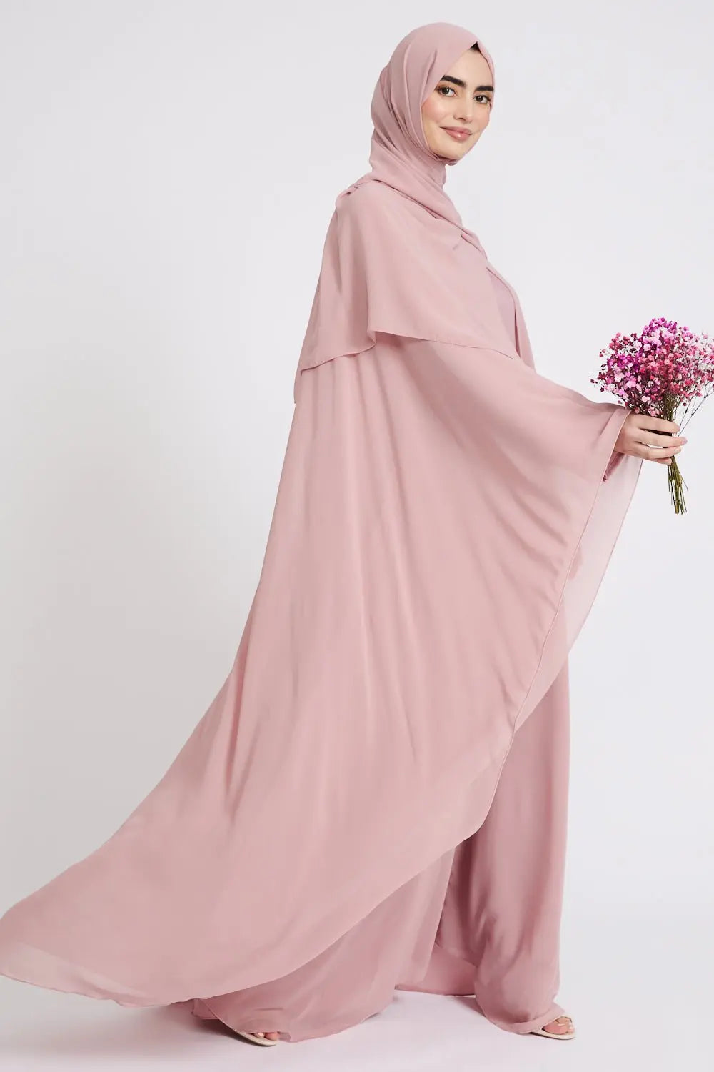 Woman wearing a pink abaya holding flowers on a white background