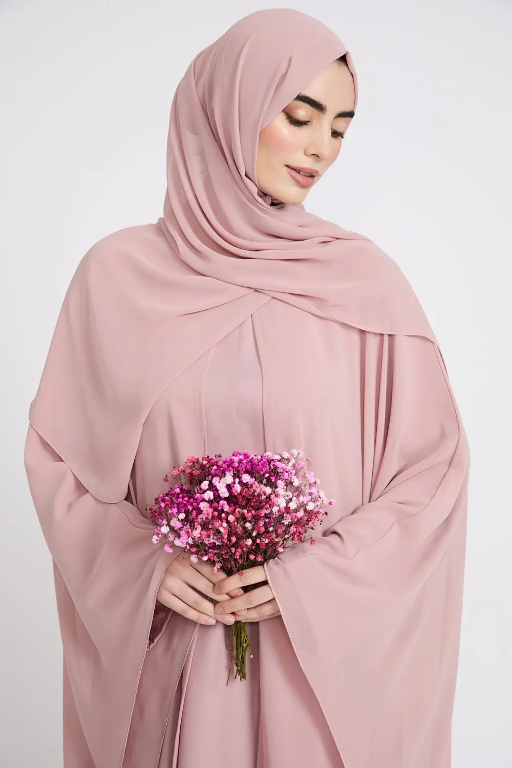Woman wearing a pink hijab and holding a bouquet of flowers against a white background