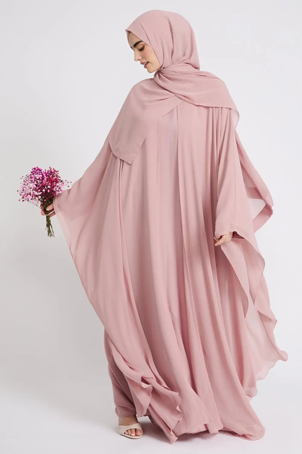Woman wearing a pink abaya with a matching hijab on a white background