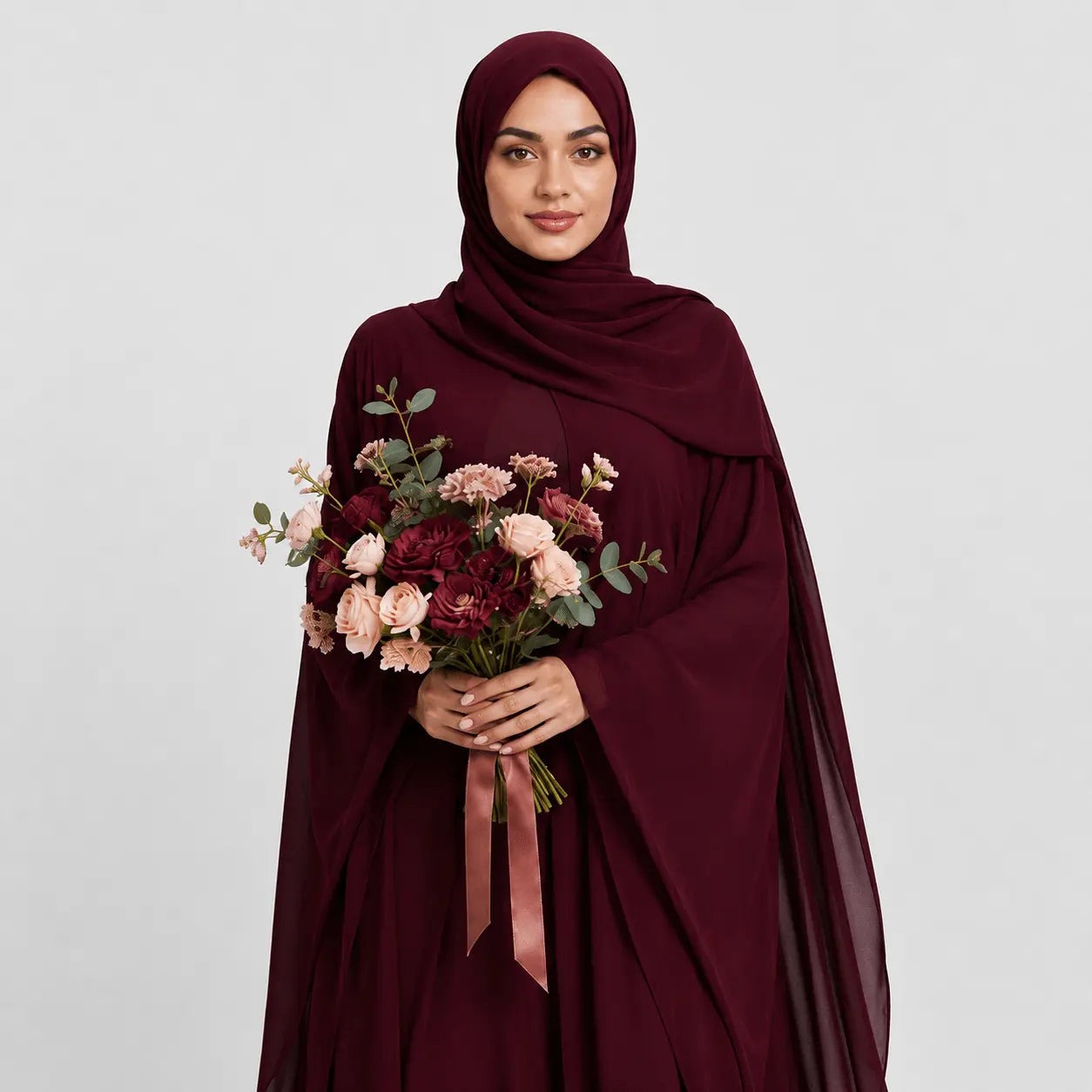 Woman in a burgundy abaya holding a bouquet of flowers on a light gray background