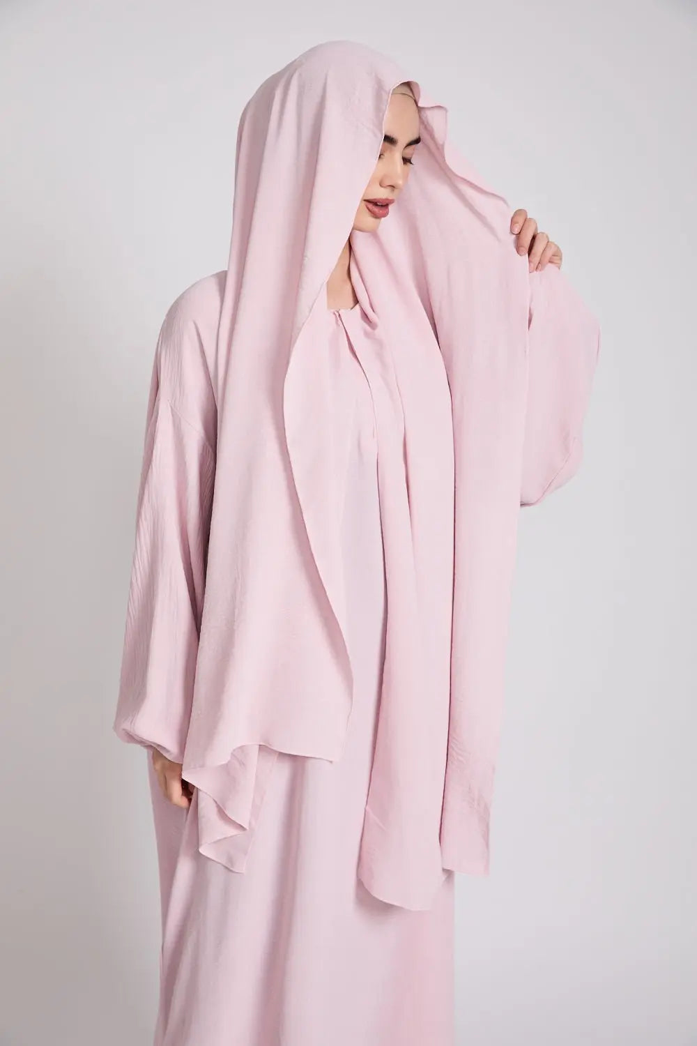 Woman wearing a light pink hijab and dress against a plain background