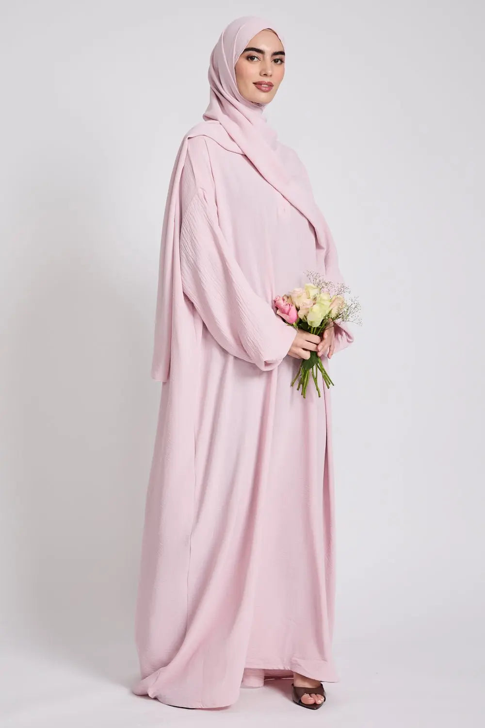 Woman wearing a light pink abaya holding flowers on a white background