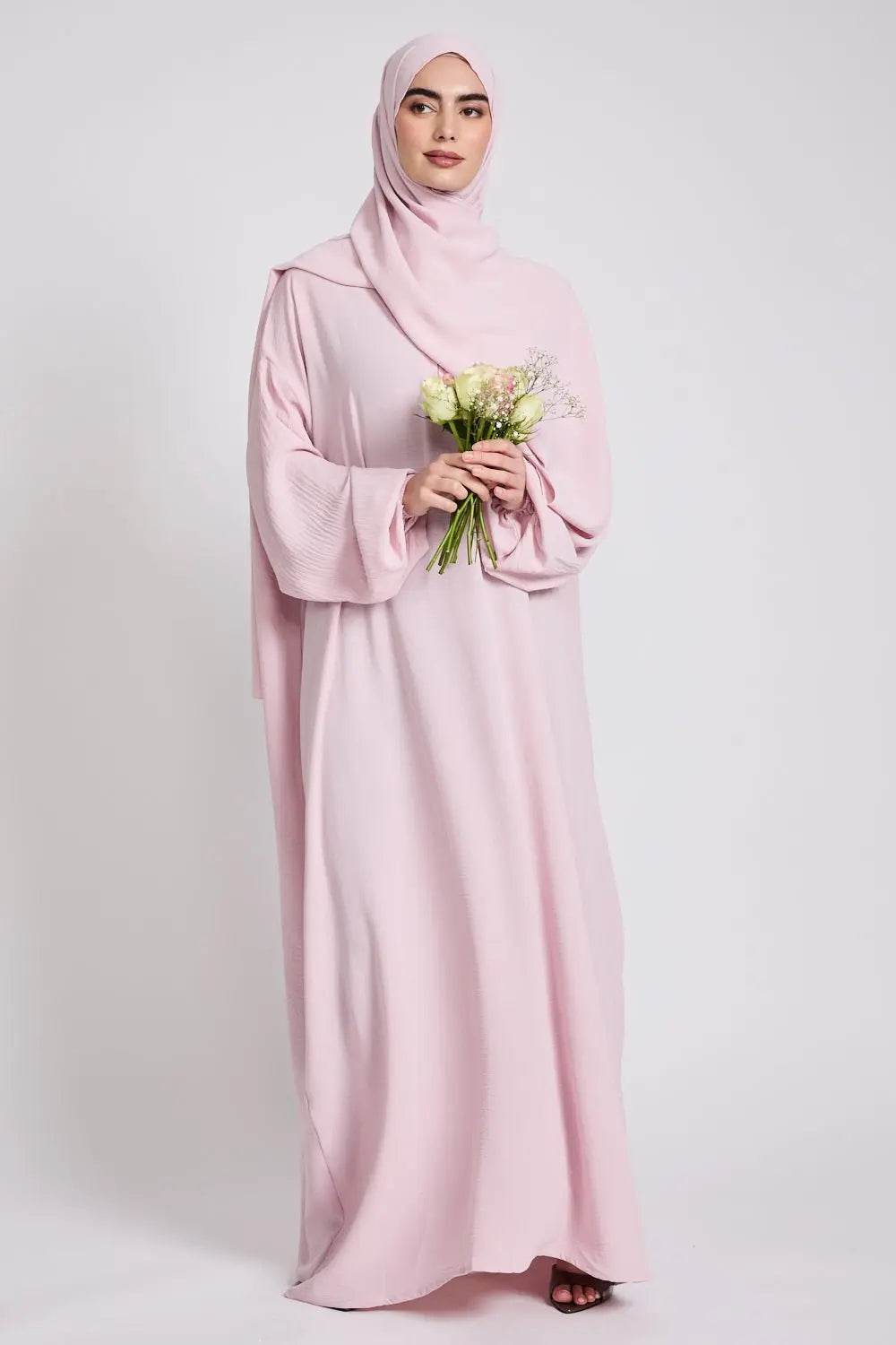Woman wearing a pink abaya holding flowers on a white background