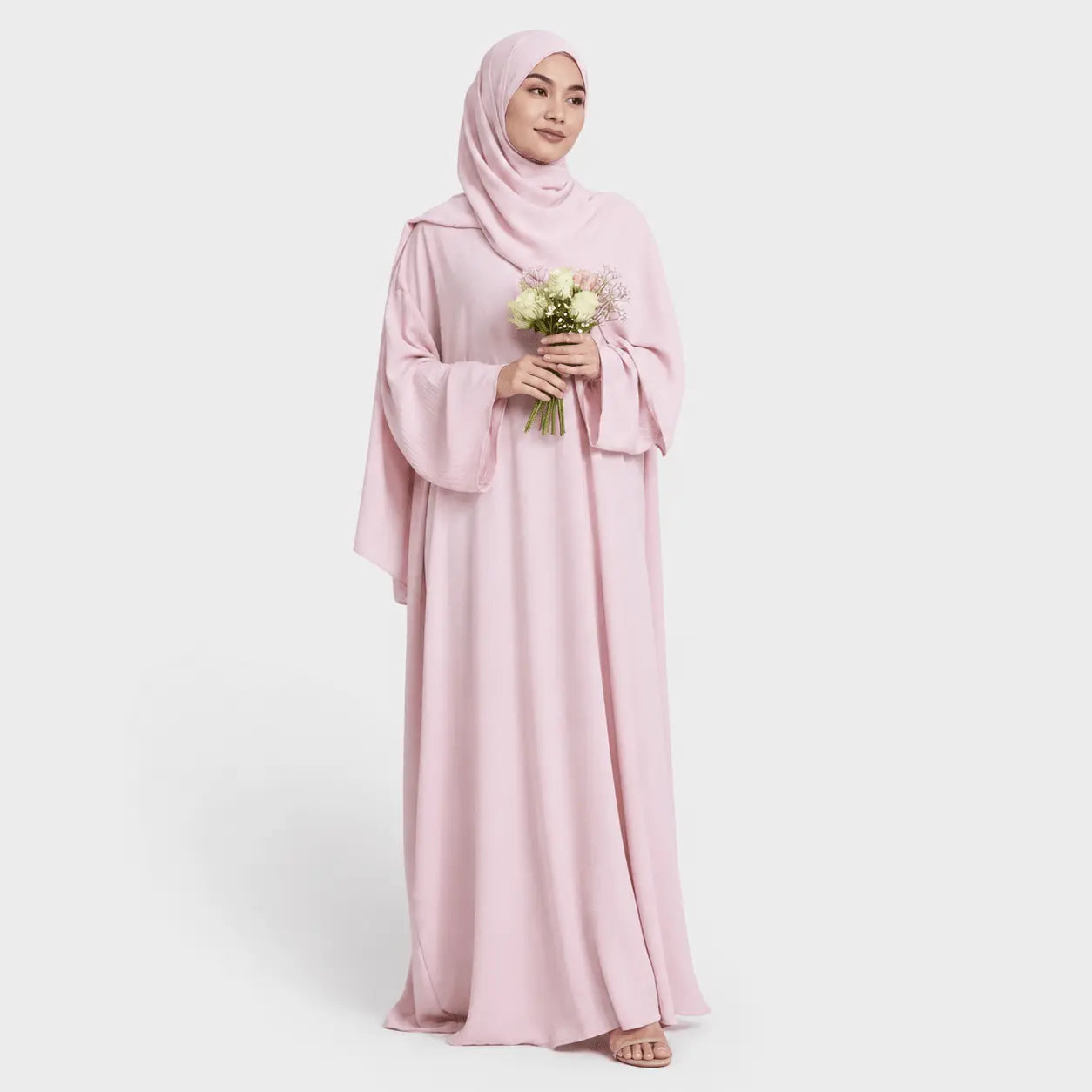 Woman wearing a pink abaya holding flowers on a white background