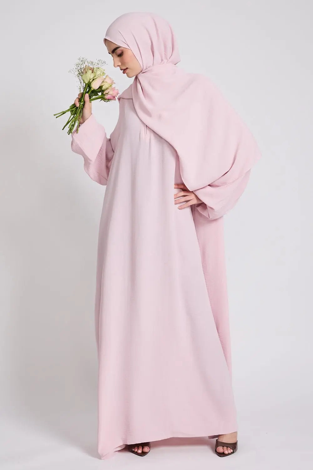 Woman wearing a pink abaya and hijab holding flowers on a white background