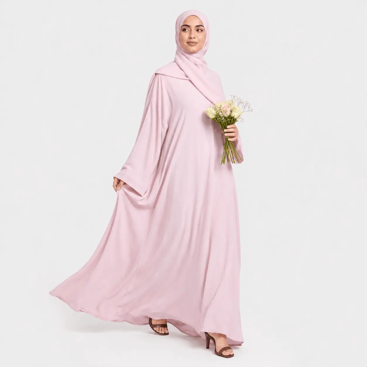 Woman wearing a pink abaya and hijab holding flowers on a white background