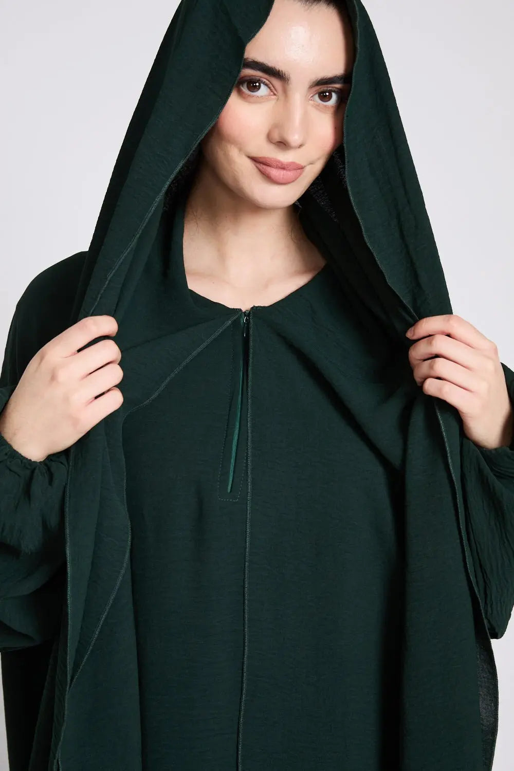Woman wearing a dark green hooded garment against a plain background