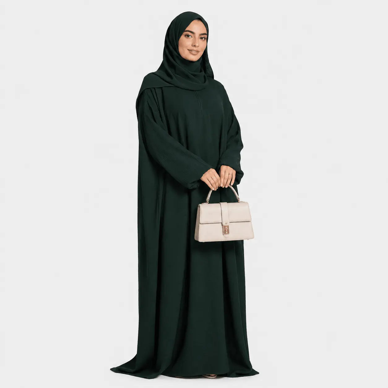 Woman wearing a dark green abaya holding a beige handbag on a white background