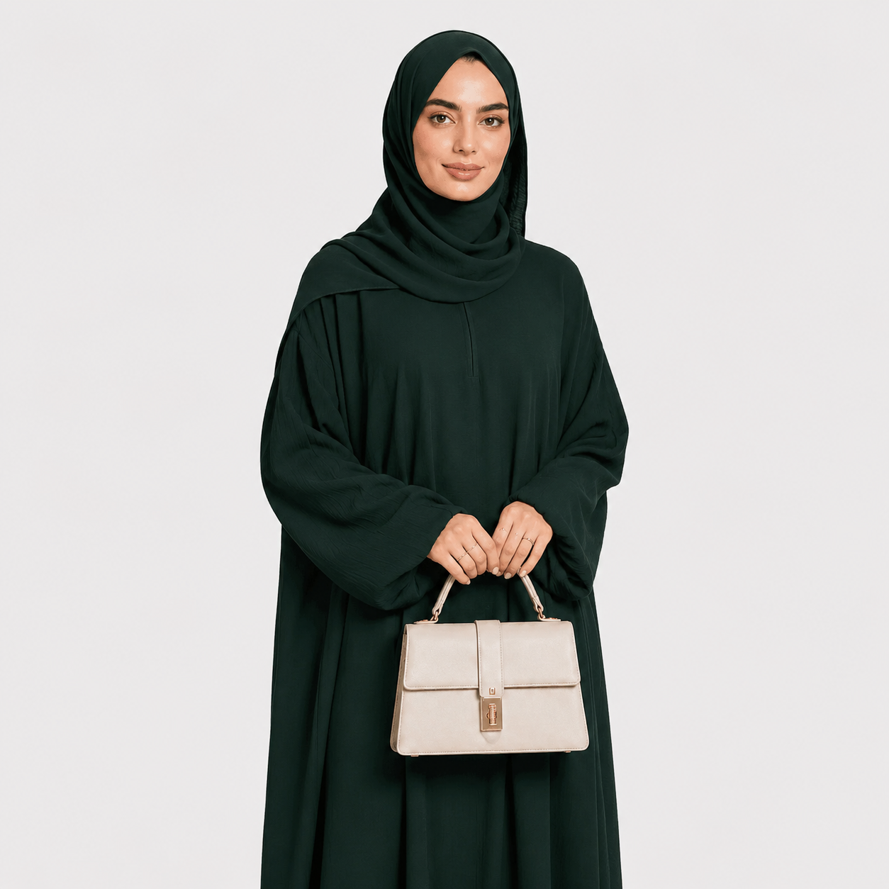 Woman in a dark green abaya holding a beige handbag against a light gray background