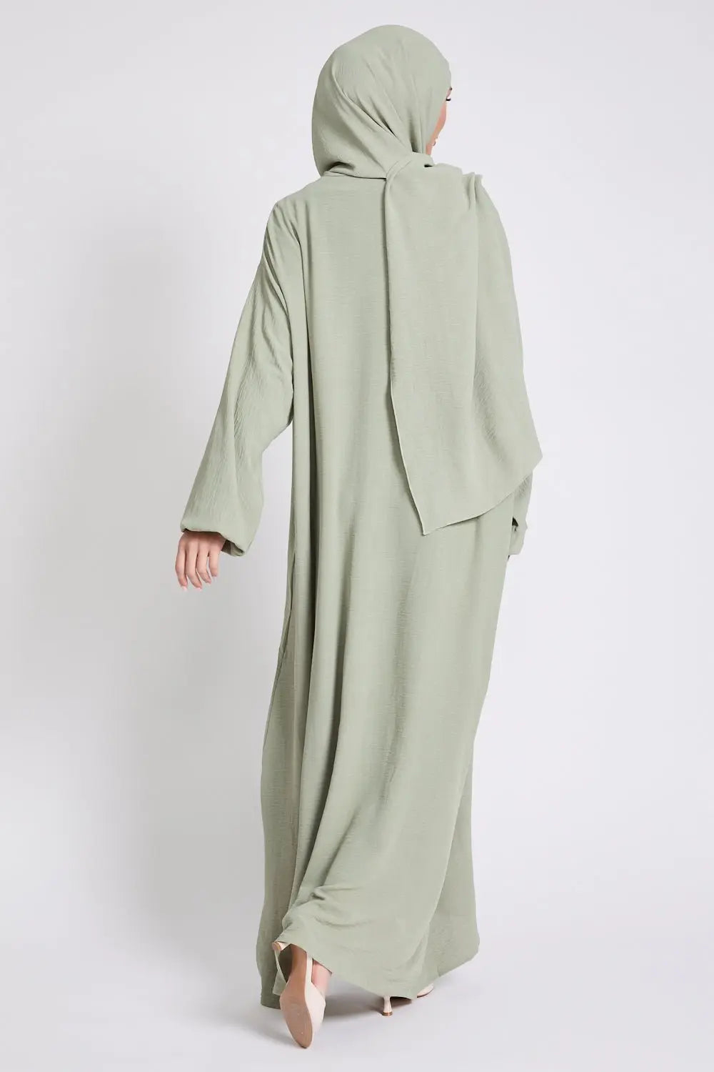 Person wearing a light green abaya with a matching hijab on a white background