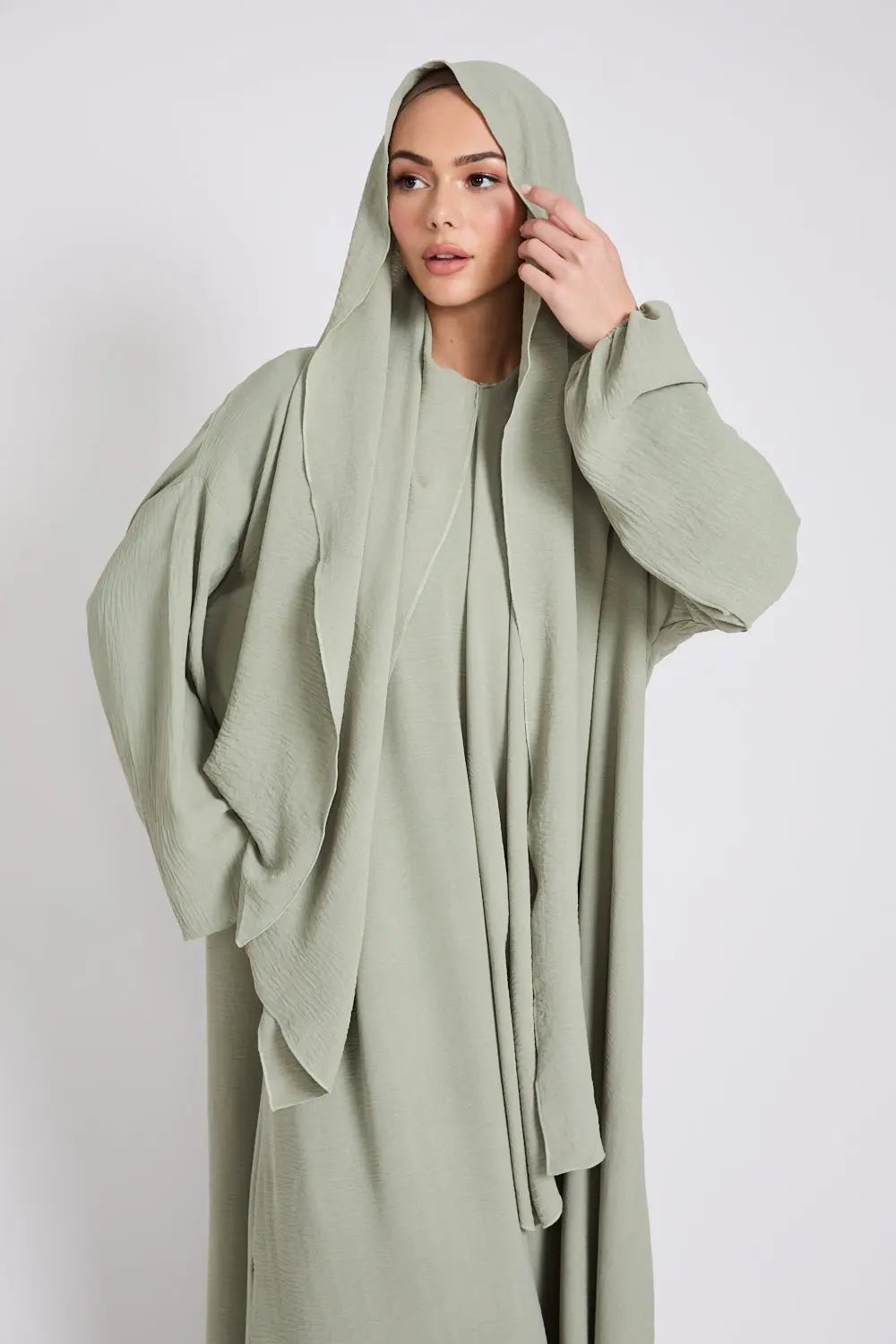 Woman wearing a light green abaya against a white background