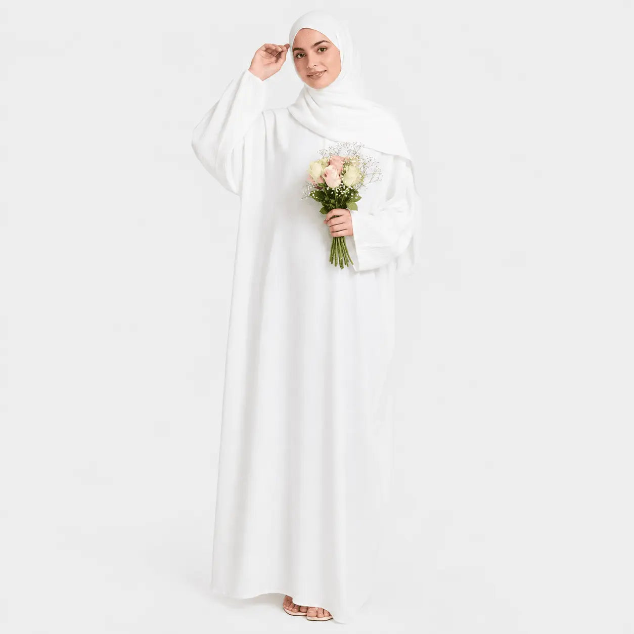 Woman in a white abaya holding flowers on a light gray background