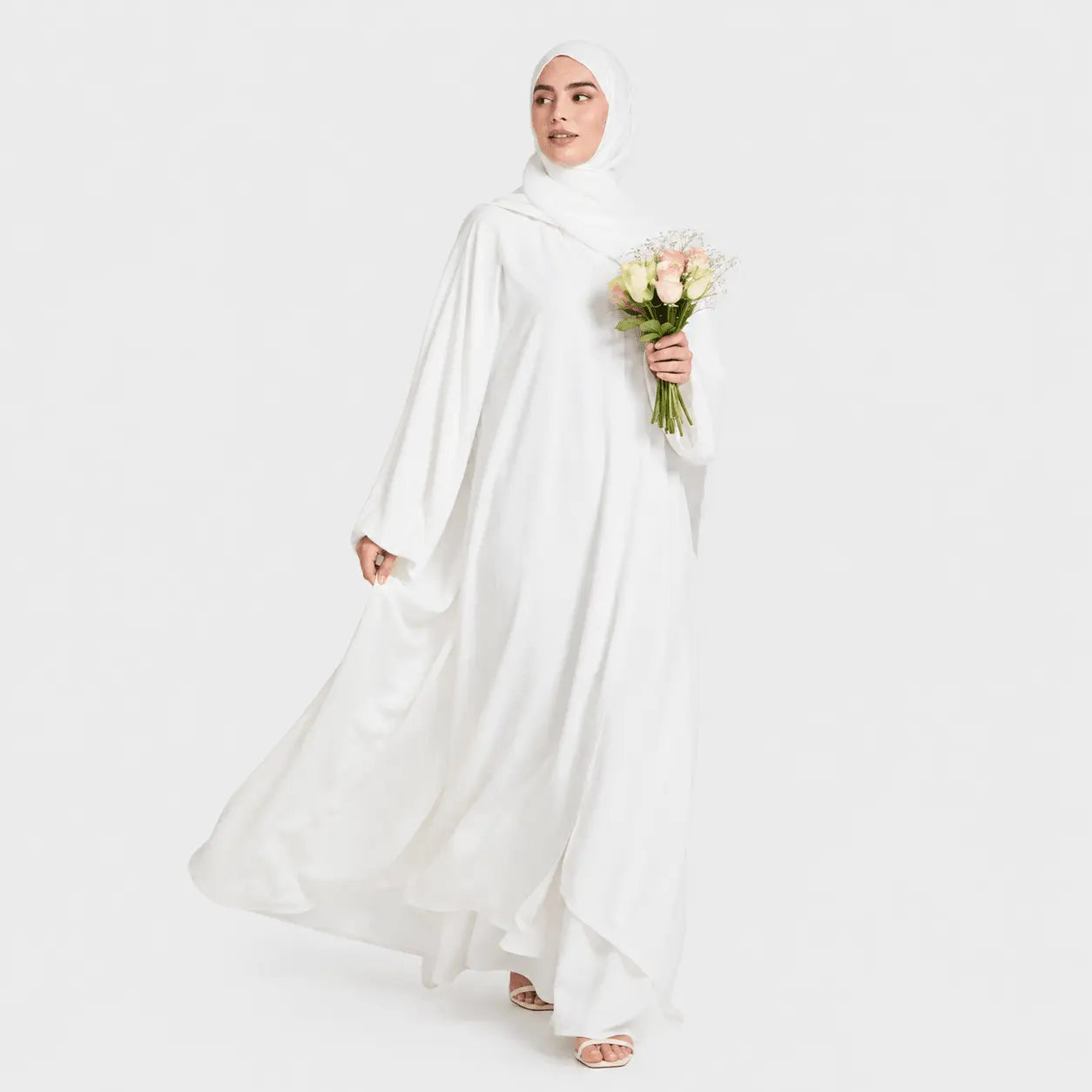 Woman in a white abaya holding flowers on a white background