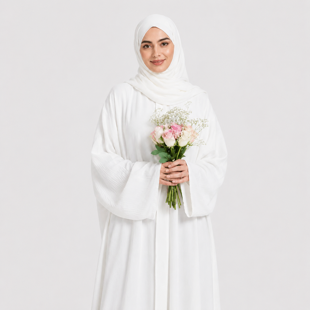 Woman in a white abaya holding flowers against a light gray background