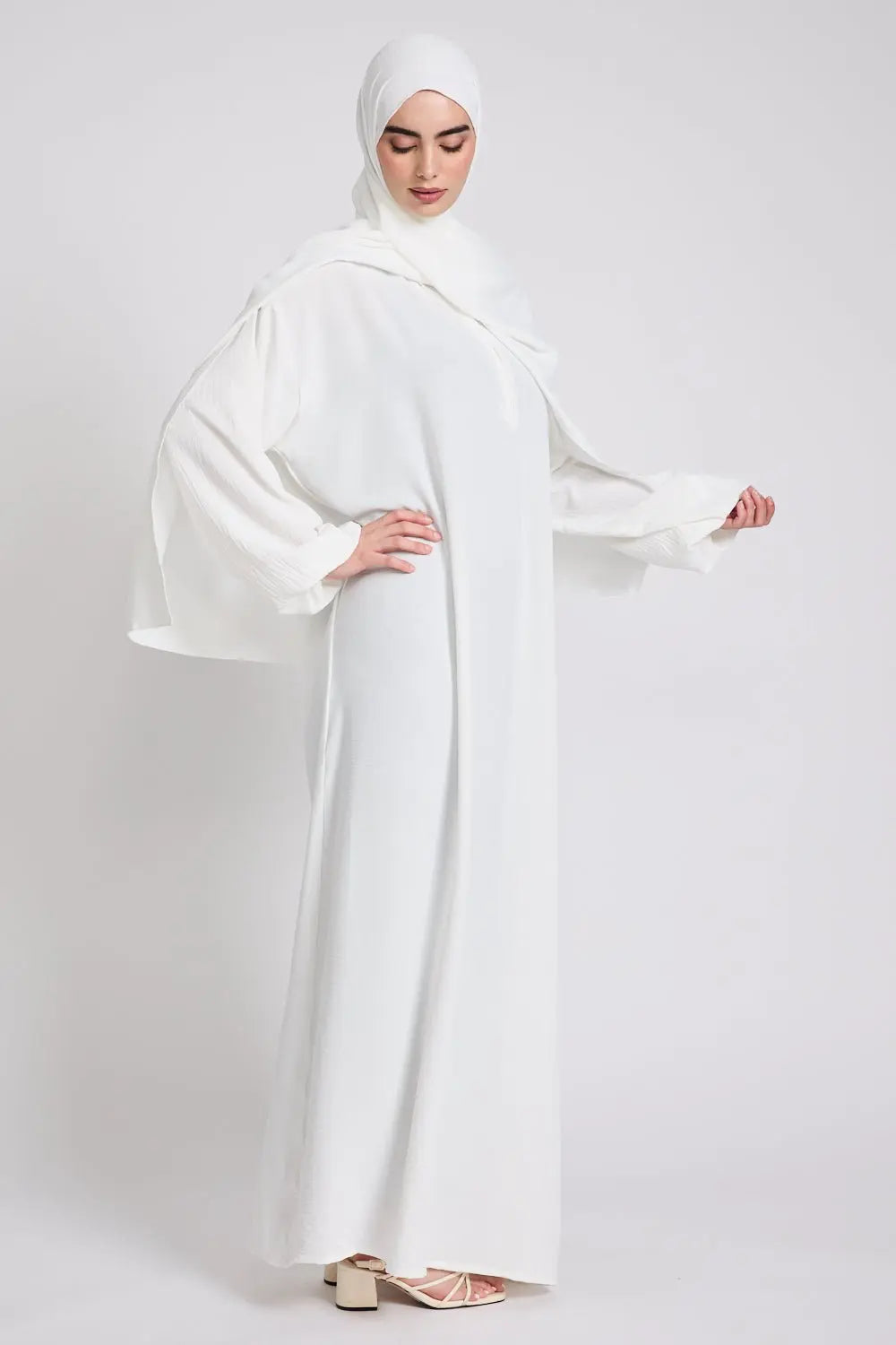 Woman wearing a white abaya on a plain background