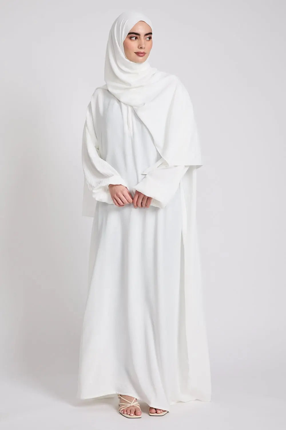 Woman wearing a white abaya and hijab on a plain background