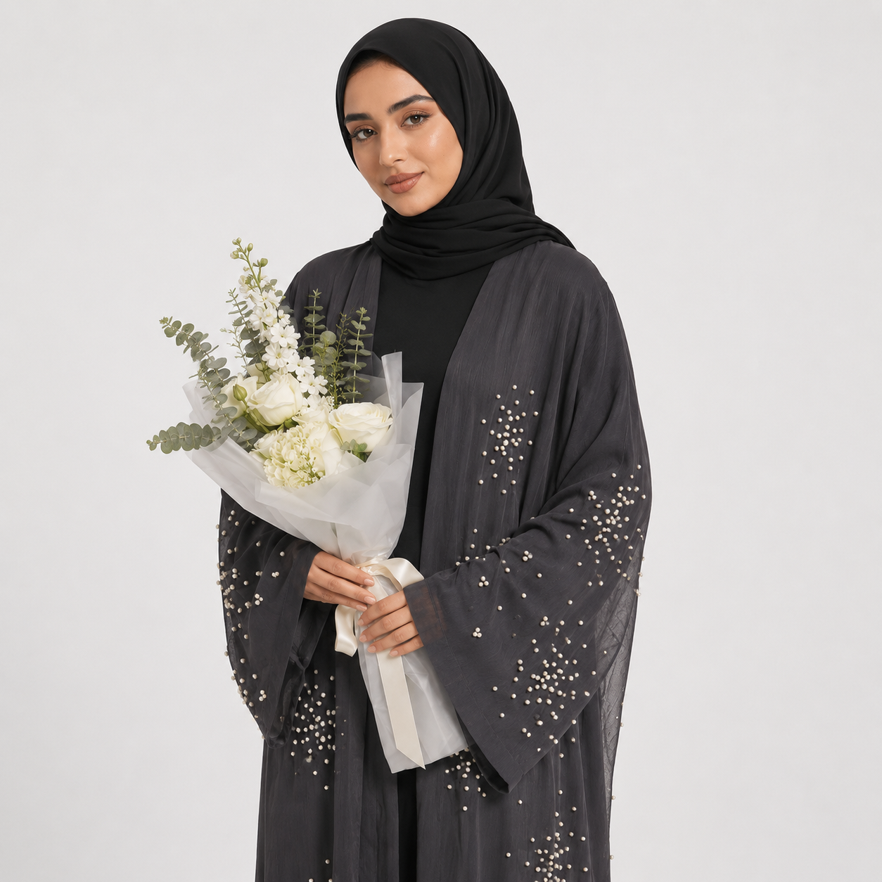 Woman wearing a black abaya with sequin details, holding a bouquet of flowers against a white background