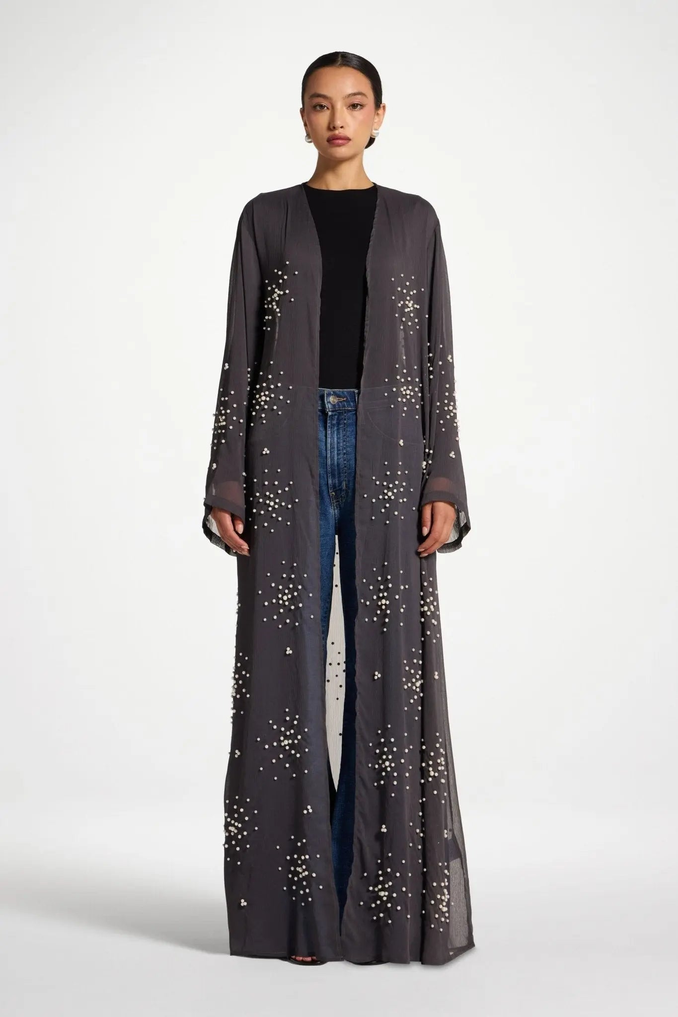 Woman wearing a long, dark gray coat with star patterns on a white background