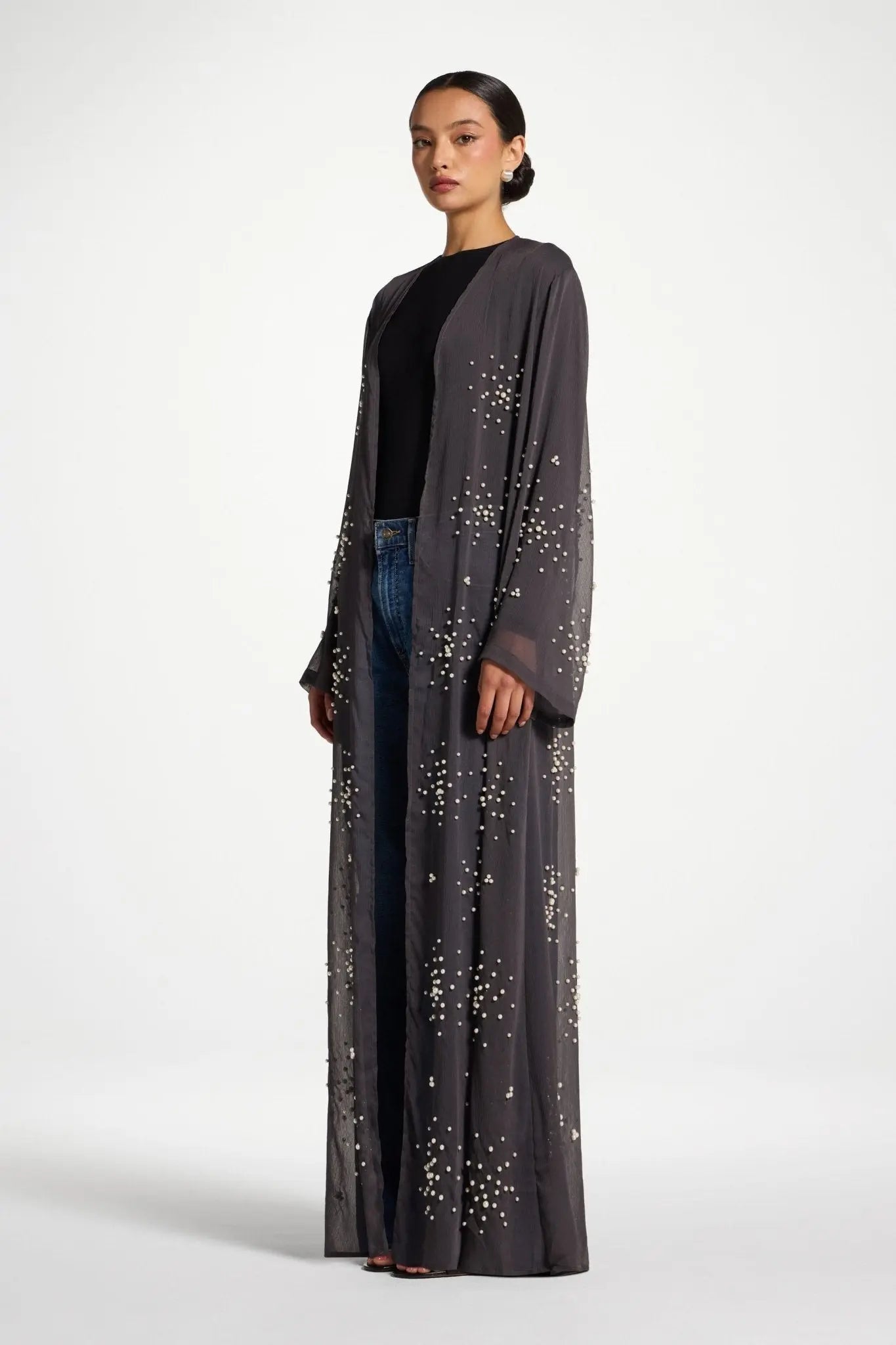Woman wearing a long, dark gray cardigan with star patterns on a white background