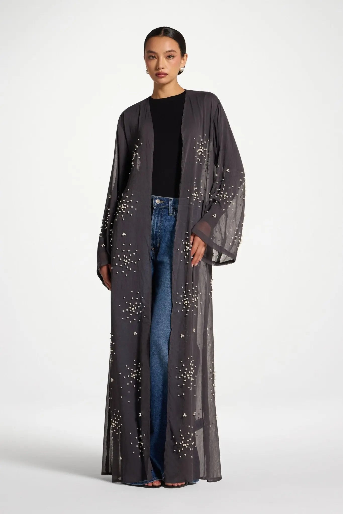 Woman wearing a long, dark gray embroidered robe over jeans on a white background